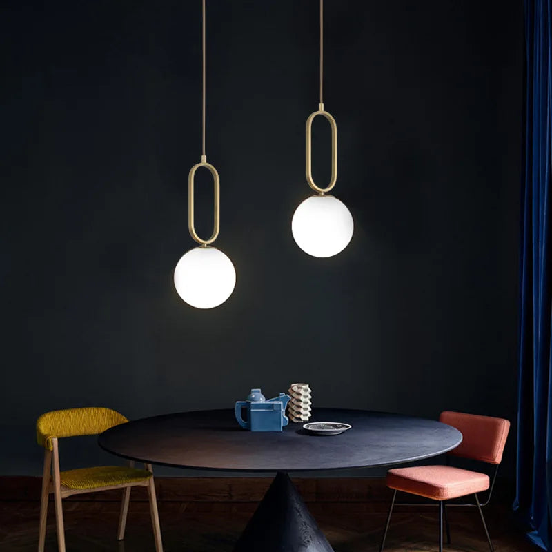 Two Lune opal globe pendants in gold oval frames above a dining table
