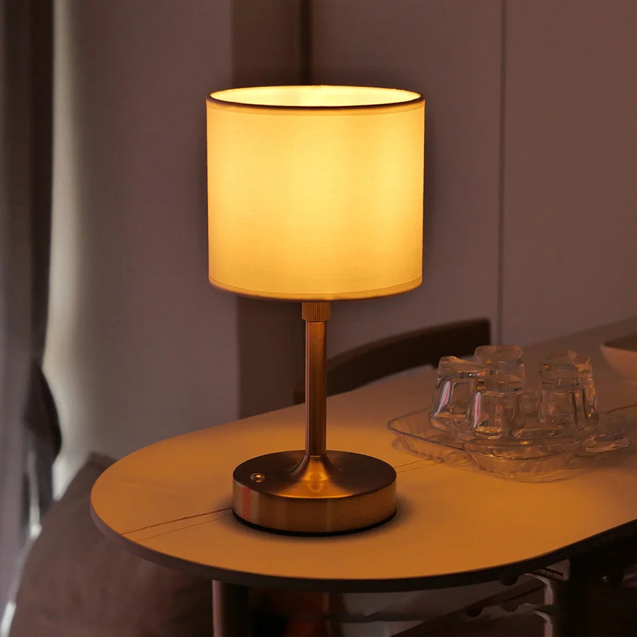 Gold Linden cordless lamp with a drum shade on a round table