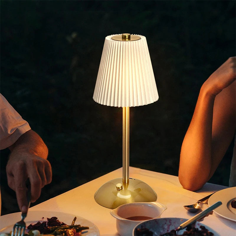 Gold Nell cordless pleated lamp glowing on a restaurant table