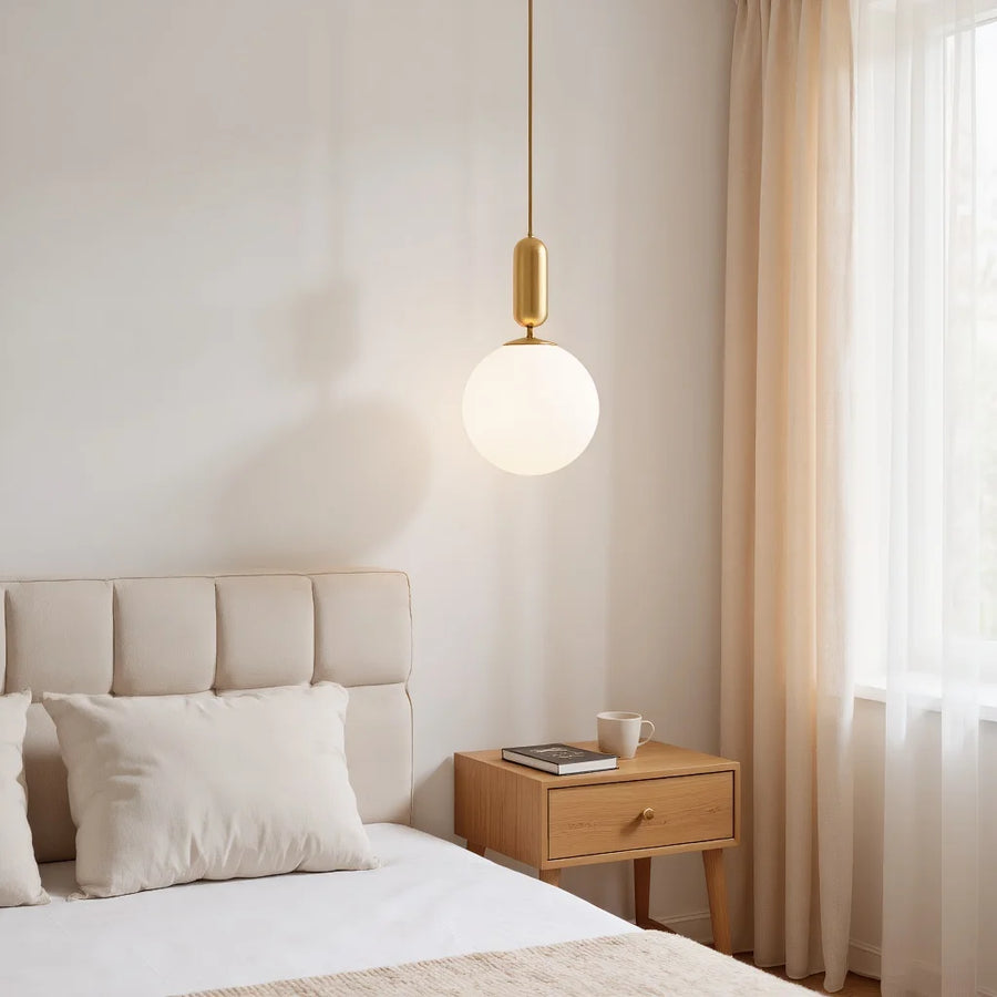 Gold Lune opal globe pendant hanging beside a neutral bed