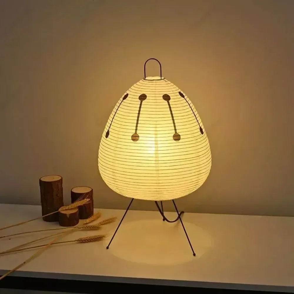 Ember Sora printed paper lantern lamp on steel tripod legs, lit on a pale surface